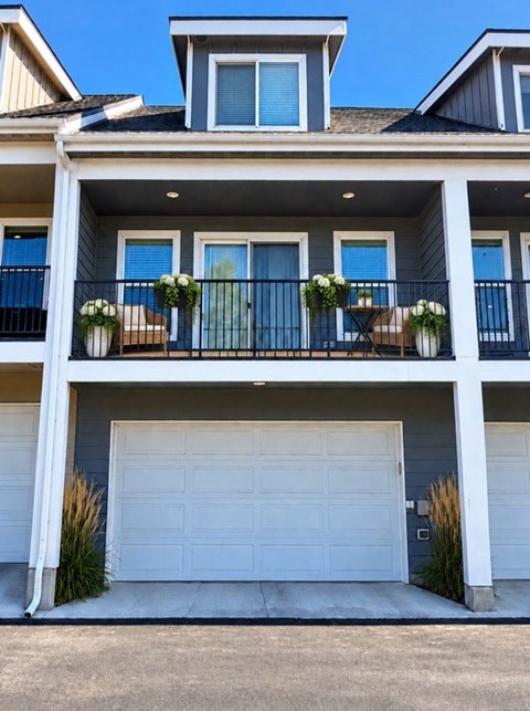 A two-story house with a white garage door and a balcony with white flower pots.