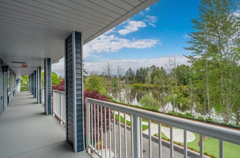 A long covered walkway with a white railing and a view of a pond and trees in the distance.