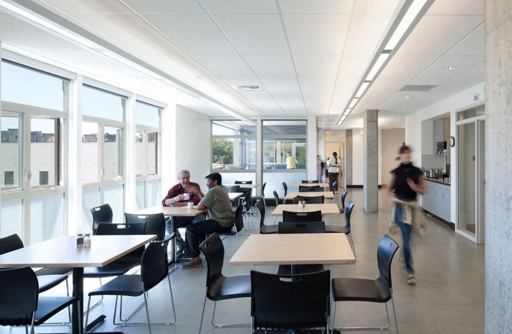 A group of people are sitting at tables in a cafeteria style dining area.