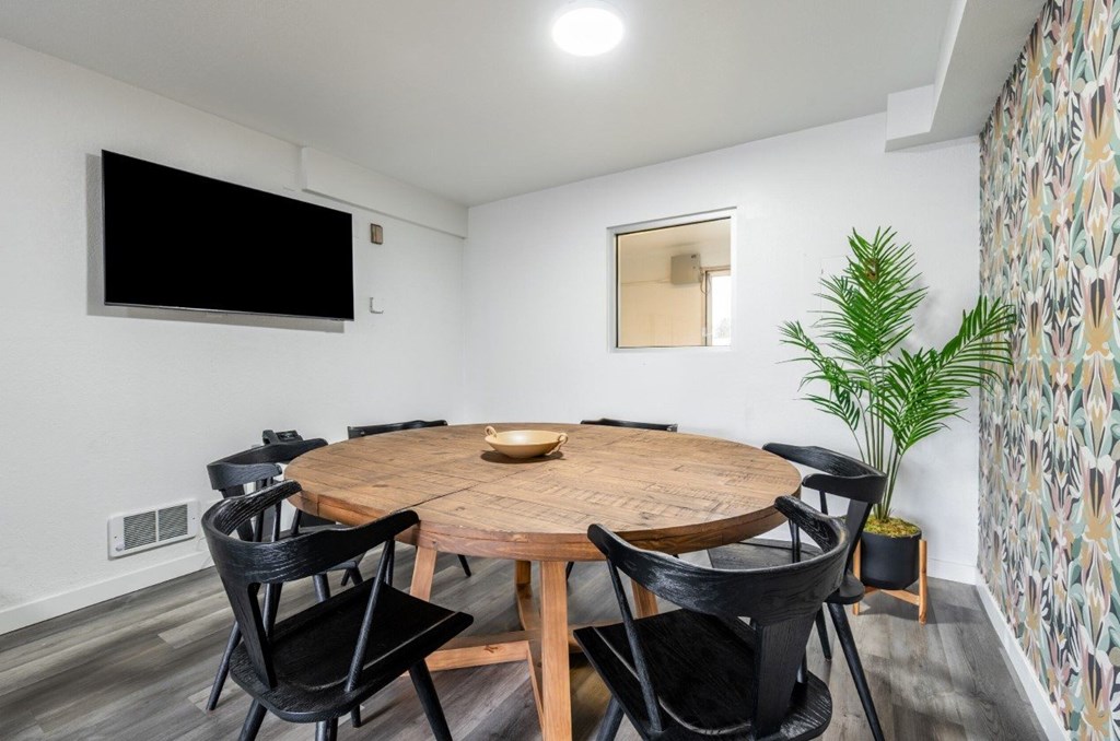 A modern dining room with a round wooden table and black chairs.