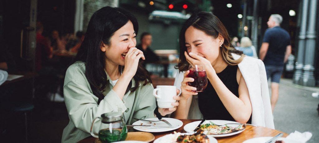 Two women laughing while eating at a table.
