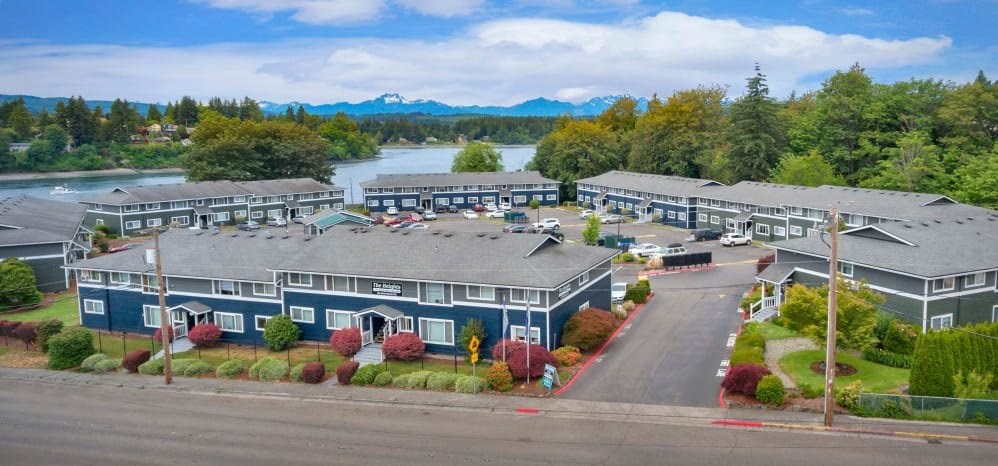 A large building complex with a parking lot in front and a lake in the background.