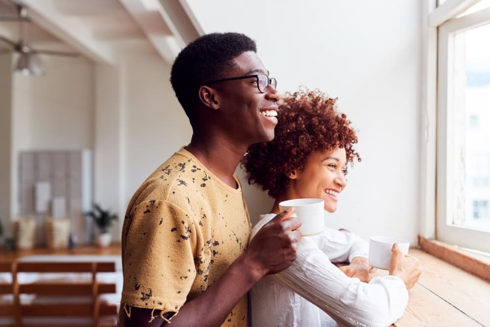 A man and a woman are standing close together, holding cups and smiling.