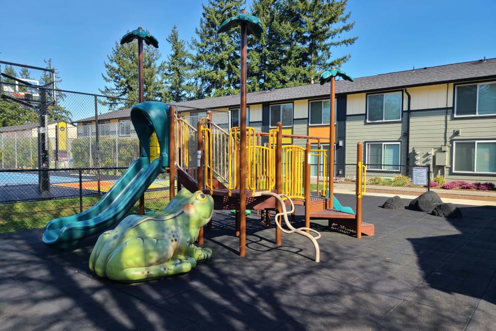 A playground with a green slide and a green frog statue.