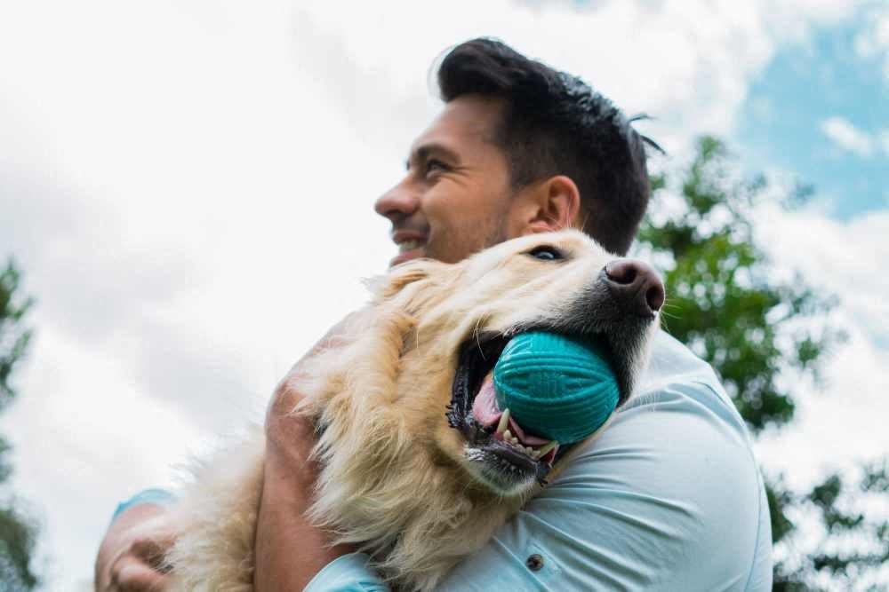 a man holding his dog with a toy in his mouth