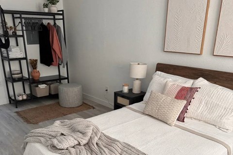 A bedroom with a bed, pillows, a clothing rack, and a rug.