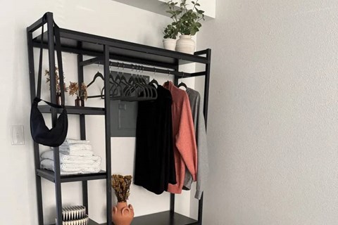 A black shelf with clothes and a potted plant.