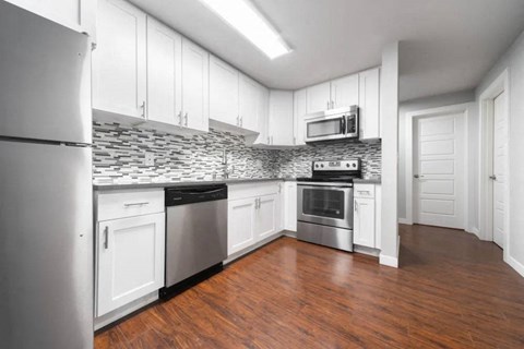A kitchen with white cabinets and a stone backsplash.