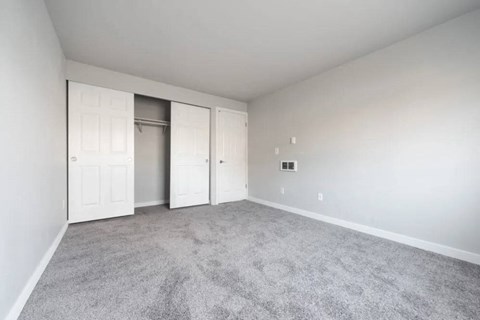 A room with grey carpet and white walls with a doorway leading to another room.