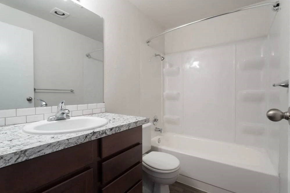 A white bathroom with a marble counter top and a white toilet.