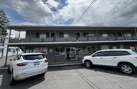 A white car is parked in front of a building with a sign that says "Now Open".