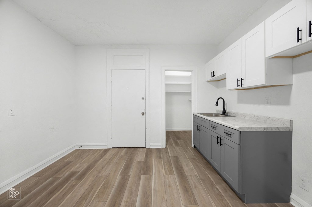 a renovated kitchen with white cabinets and gray countertops and a door to a closet