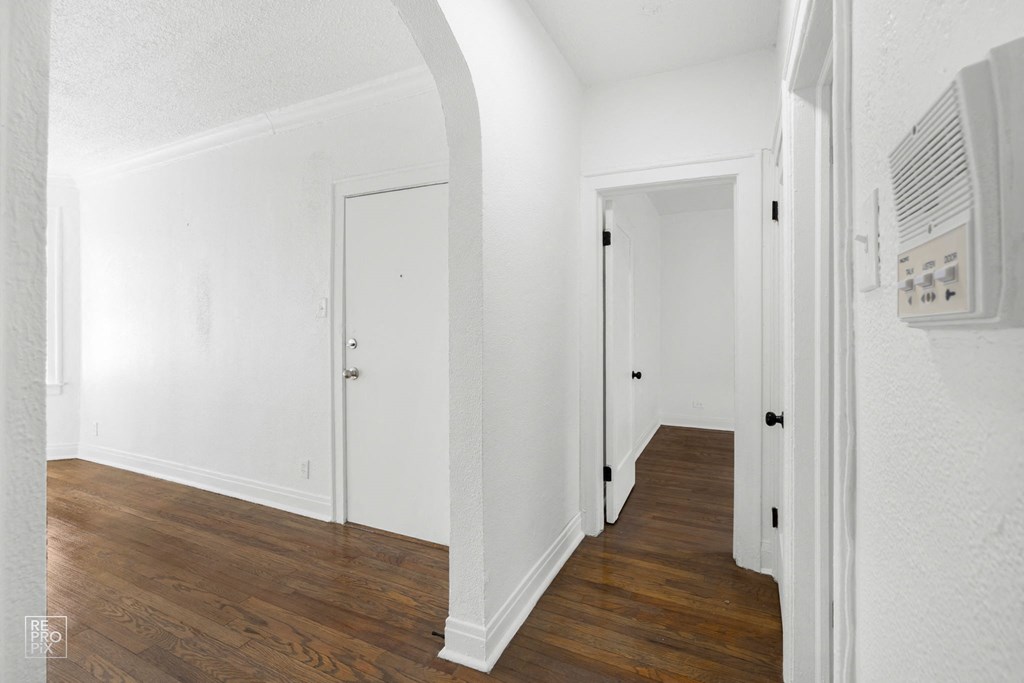 a bedroom with white walls and wood floors and a hallway with white doors
