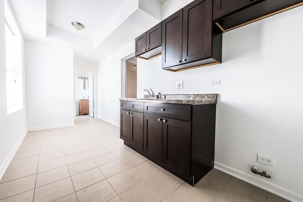 a kitchen with black cabinets and white walls and tiled floors