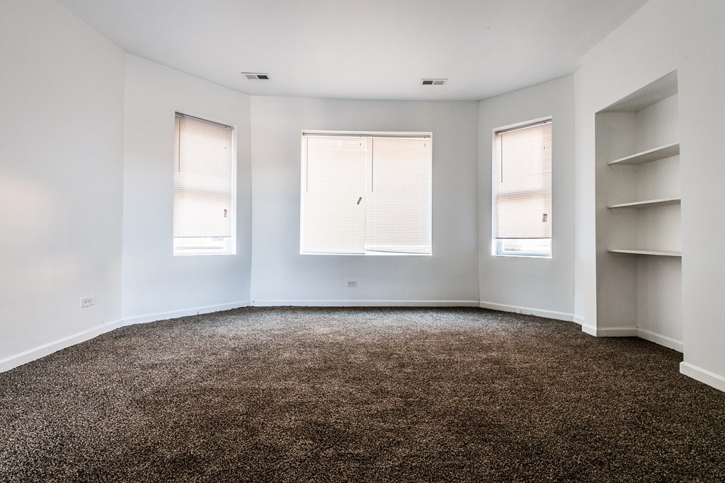 an empty room with three windows and white shelves