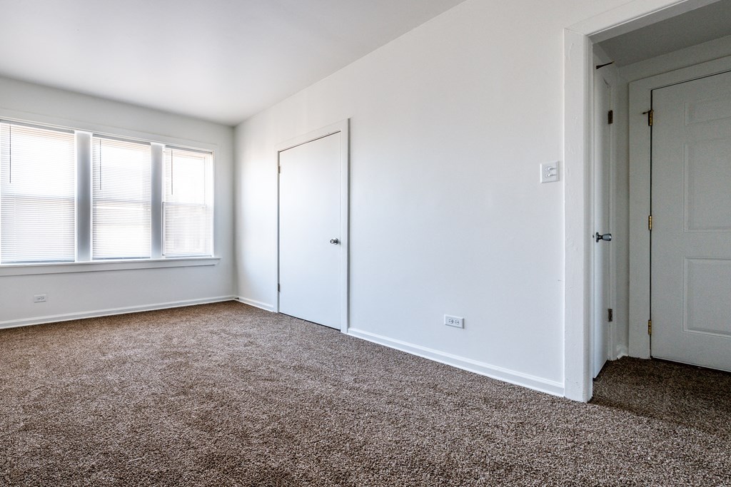a bedroom with white walls and carpet and a door and window