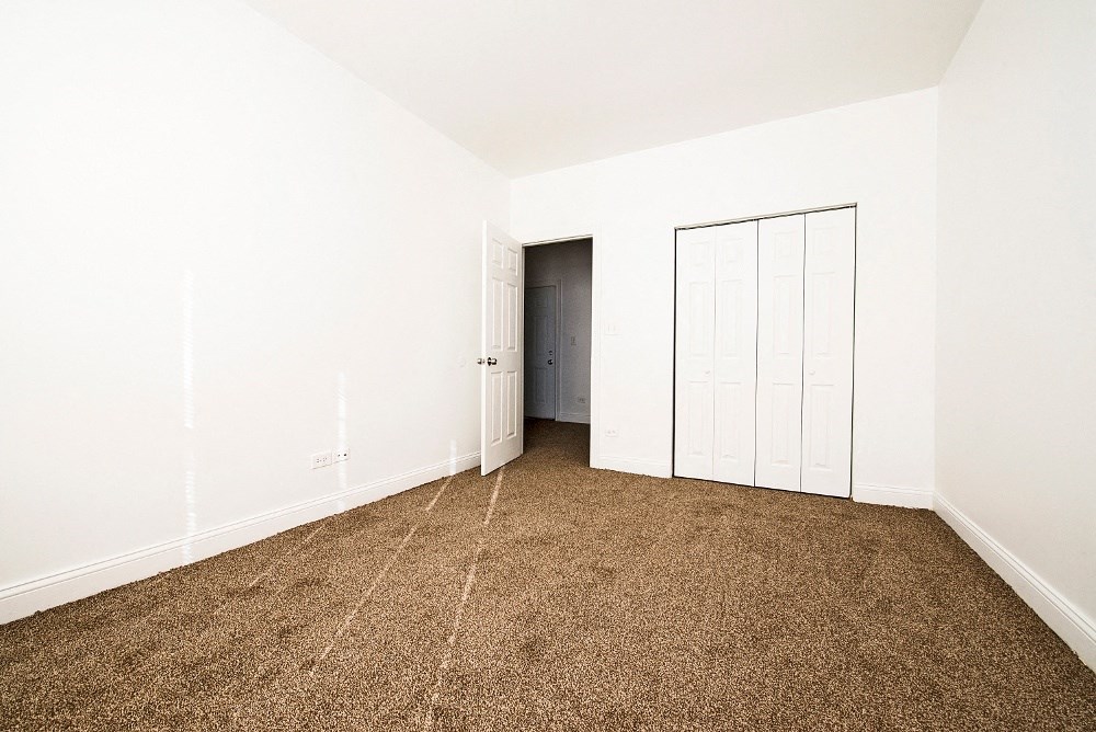 a master bedroom with carpet and white walls and a closet