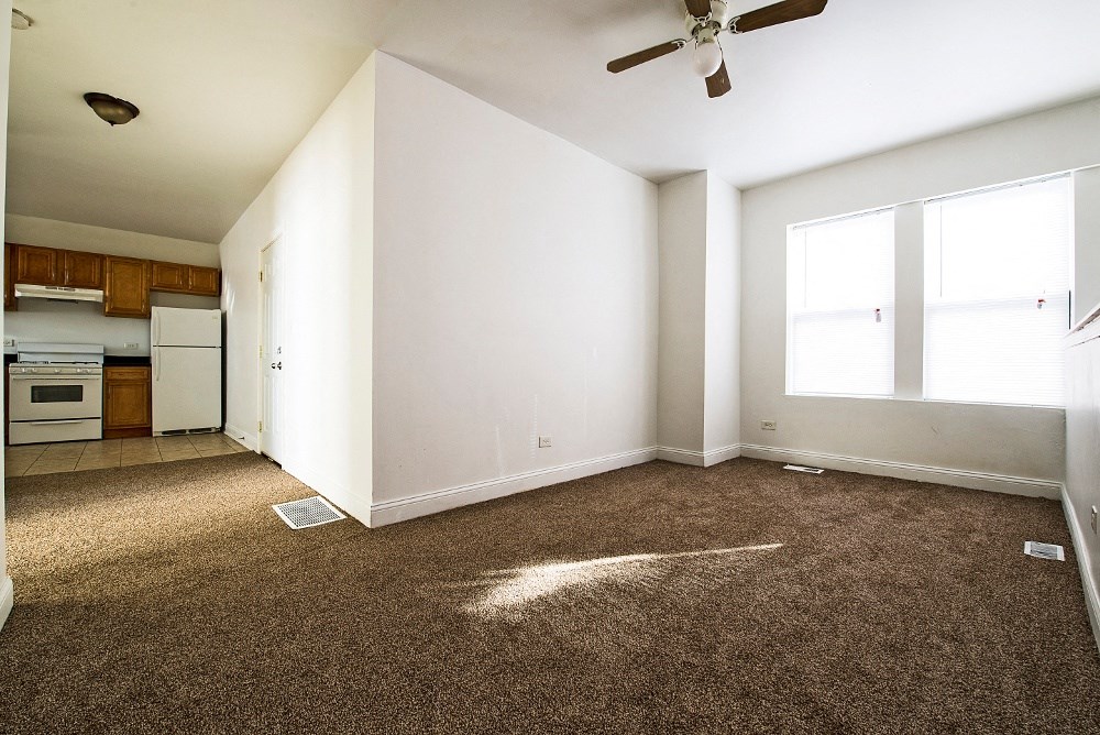 an empty living room with a ceiling fan and a kitchen