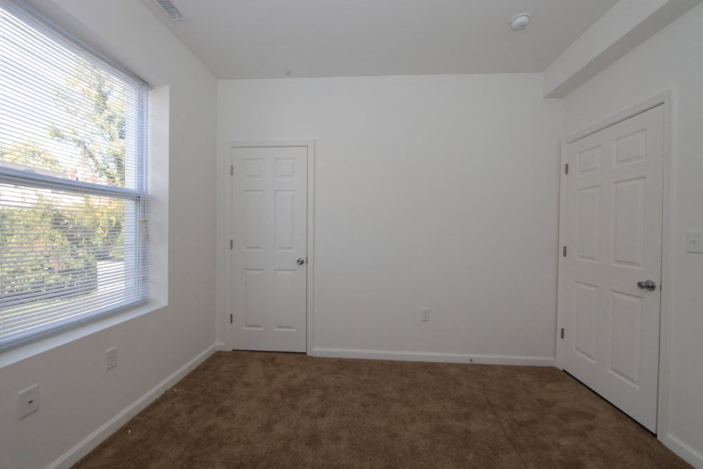 a bedroom with a window and two doors and a carpet