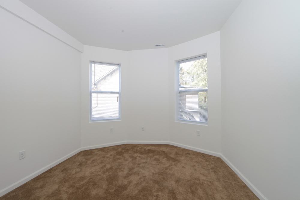 an empty room with two windows and a brown carpet