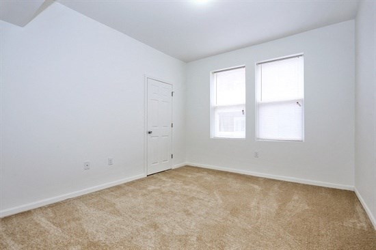 an empty living room with a door and two windows