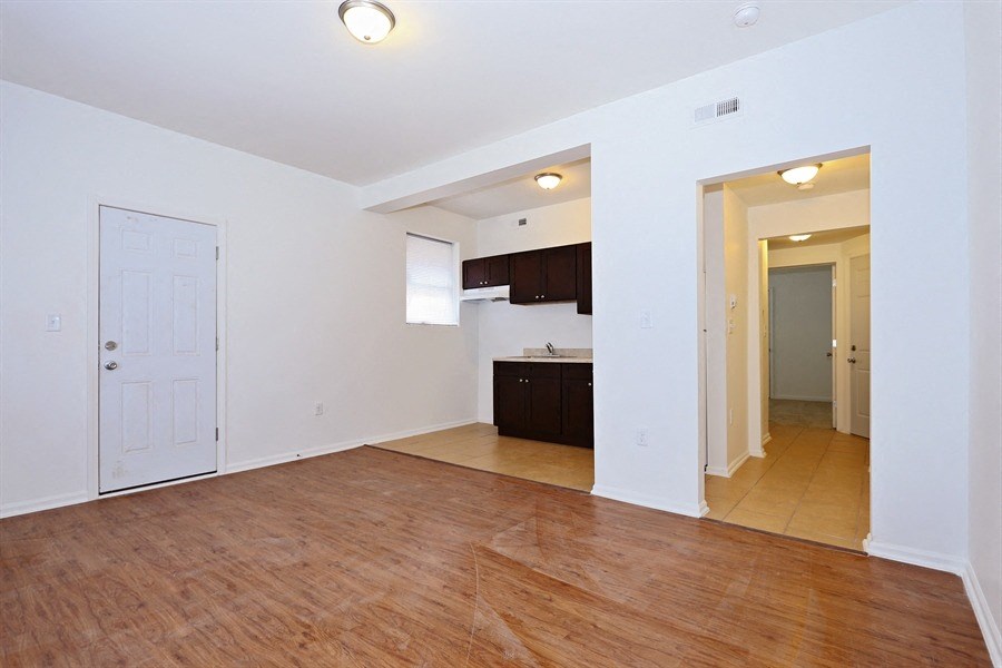 an empty living room and kitchen with wood flooring and white walls