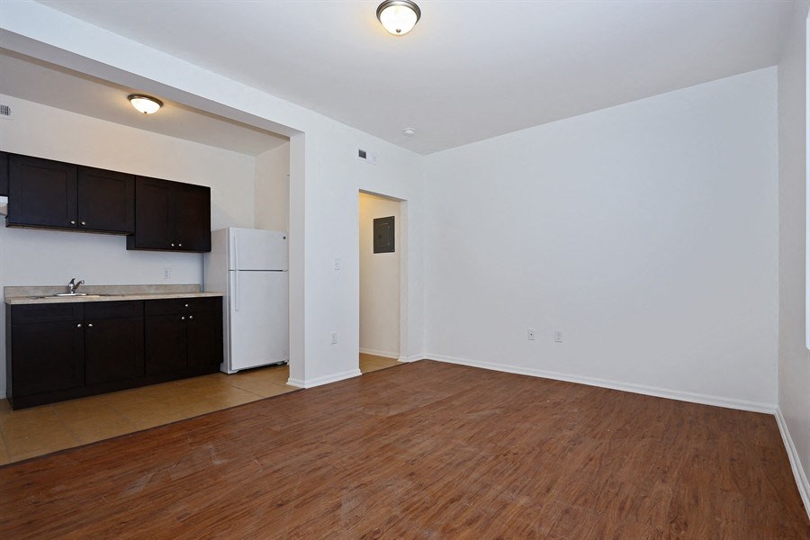 the living room and kitchen of an apartment with wood flooring and a refrigerator