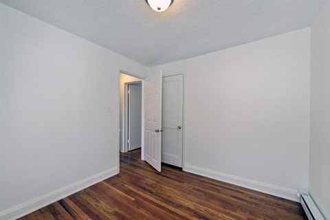 a bedroom with white walls and wood flooring and a closet
