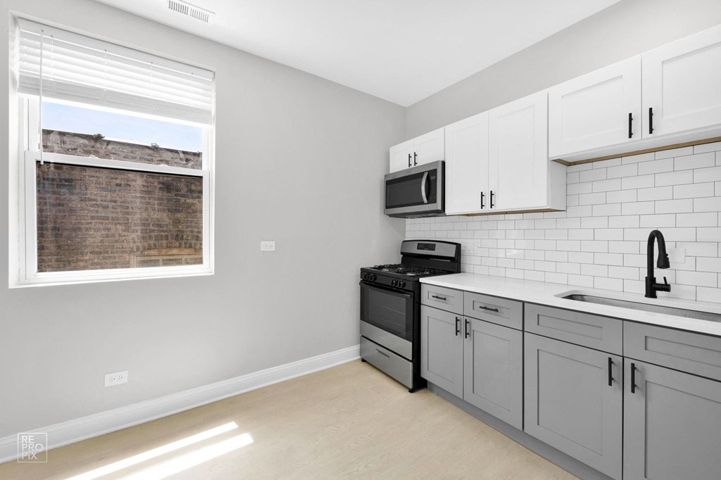 a kitchen with white cabinets and gray counters and a window with a view of a brick building