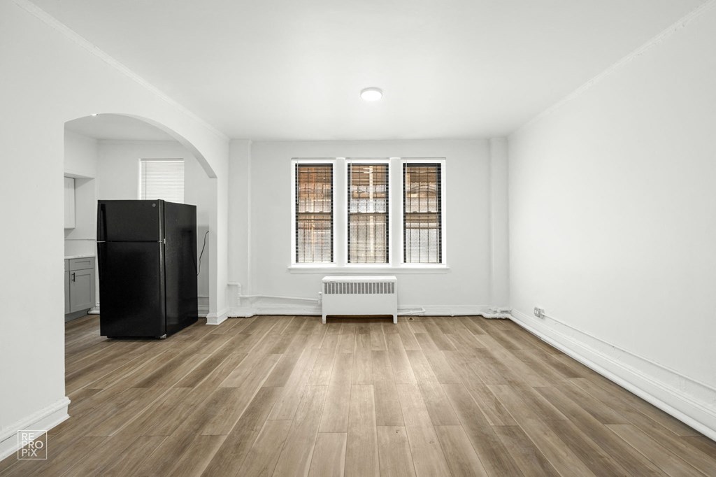 a living room with white walls and wood floors and a black refrigerator