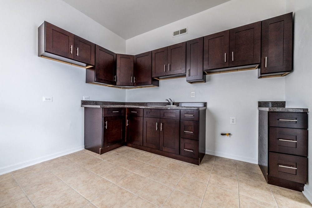 an empty kitchen with dark wood cabinets and tile flooring
