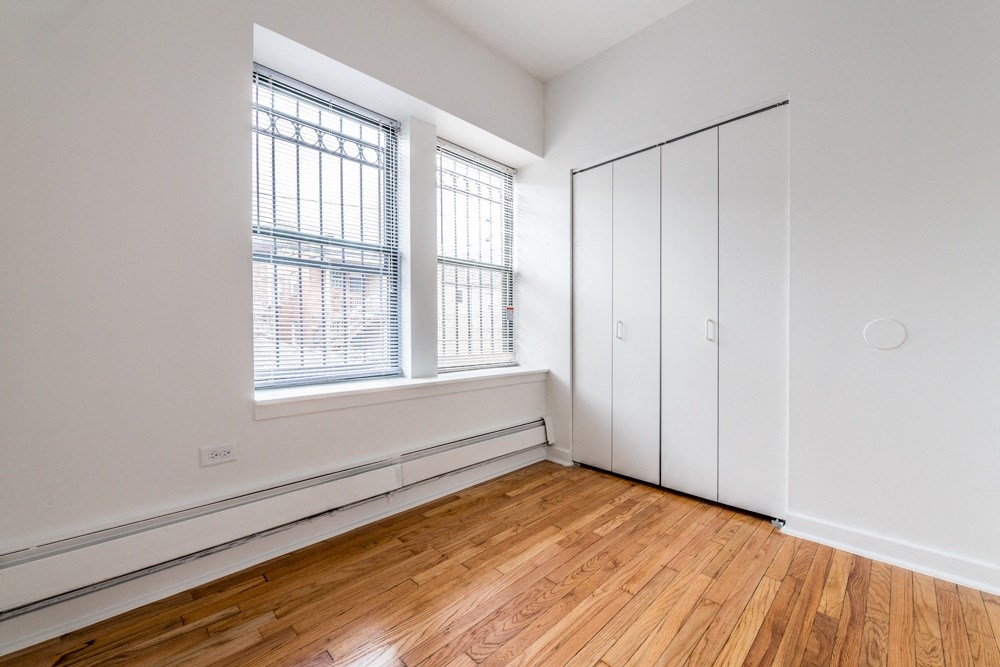 a bedroom with white walls and wood floors and a closet
