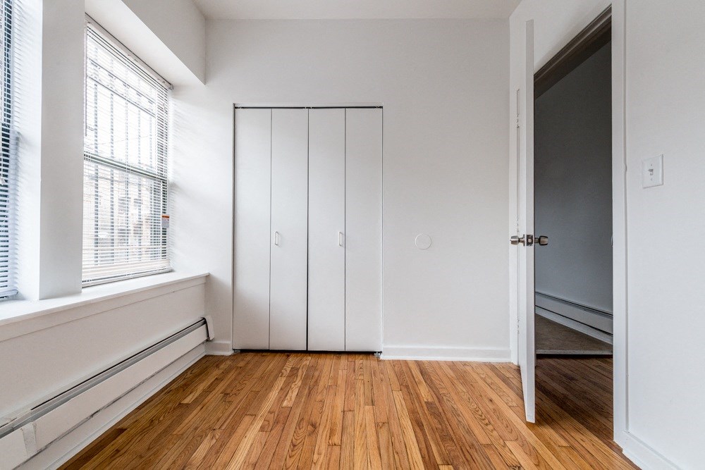a bedroom with white walls and wood floors and a closet