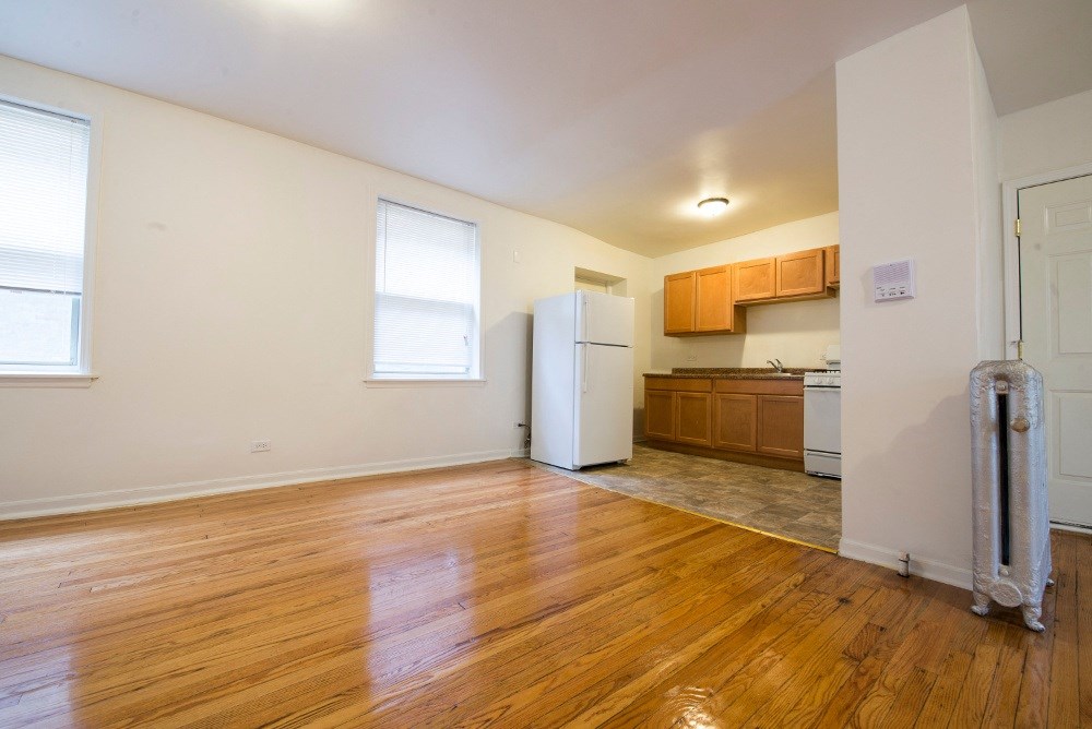 an empty living room and kitchen with wood floors and a refrigerator