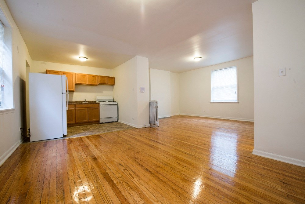 the living room and kitchen of an empty apartment with wood flooring and white walls