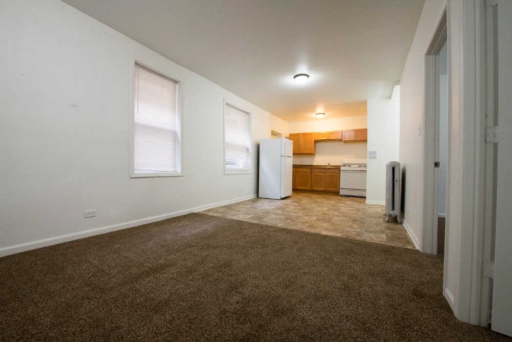 an empty living room with a kitchen in the background