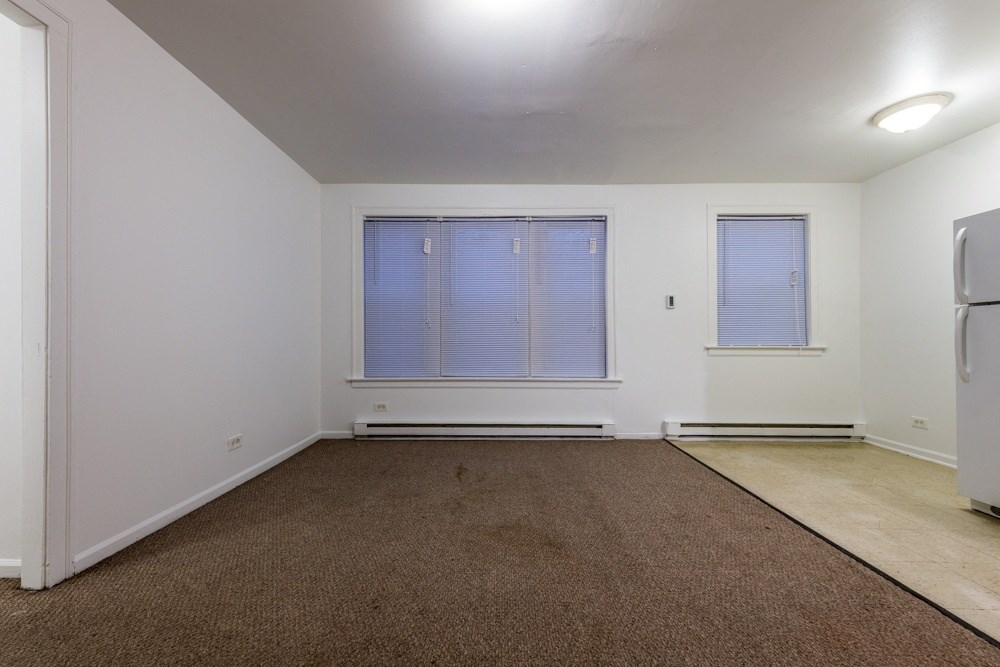 an empty living room with a refrigerator and a window