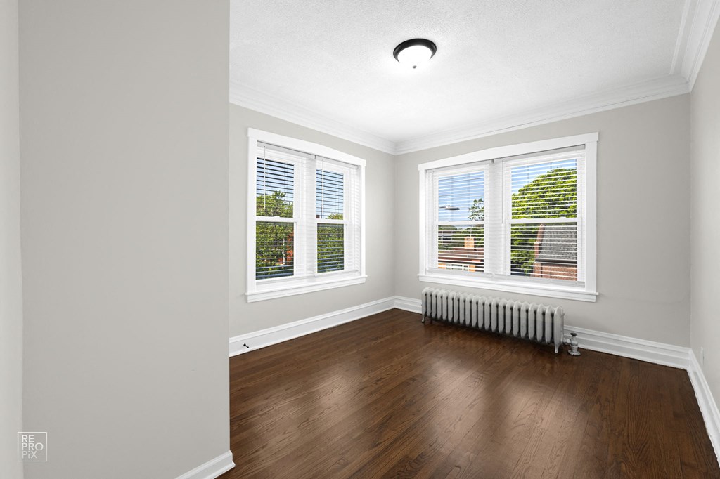 a bedroom with hardwood floors and three windows