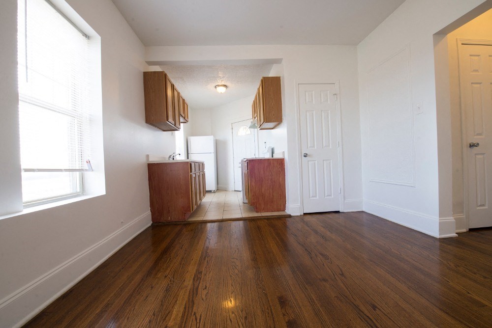 an empty living room with wood flooring and a door to a kitchen