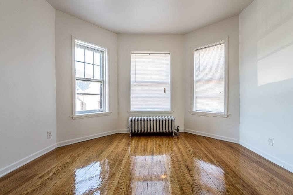 an empty living room with a radiator and three windows