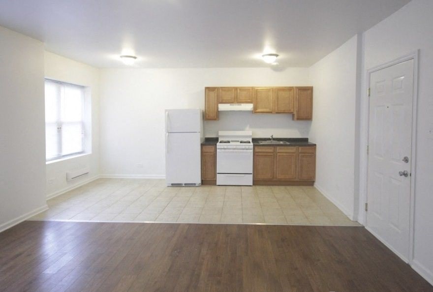 an empty kitchen and living room with wood floors and white appliances