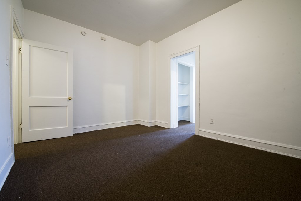 a bedroom with white walls and carpet and a door to a closet