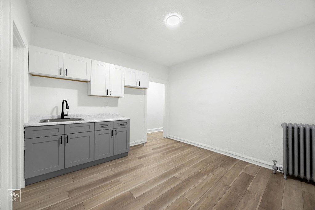 the living room and kitchen of an apartment with white cabinets and wood flooring