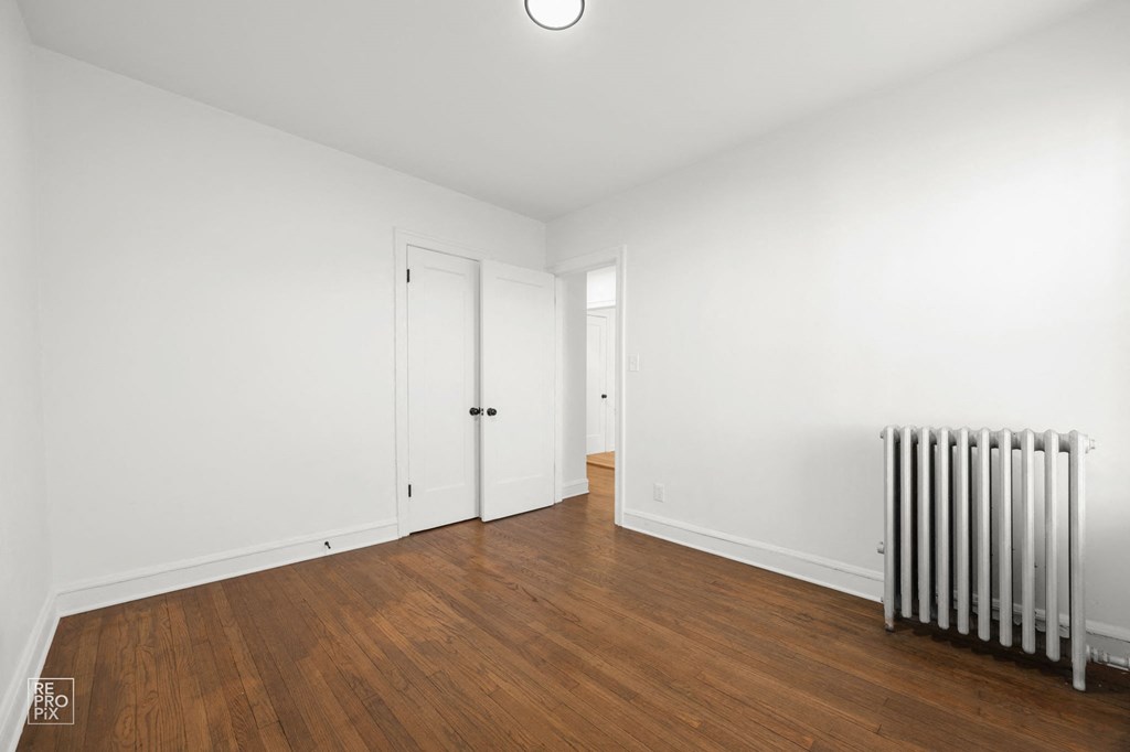 a bedroom with white walls and wood floors and a radiator