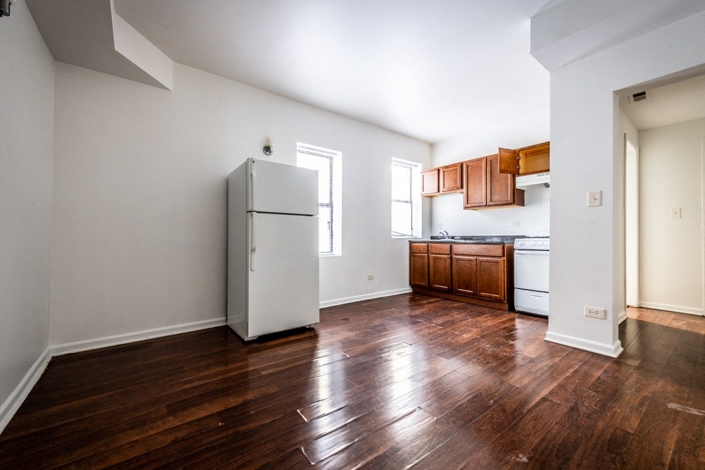 an empty living room with a refrigerator and a kitchen
