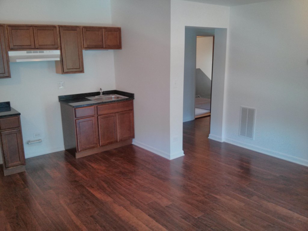 an empty living room with wooden floors and a kitchen