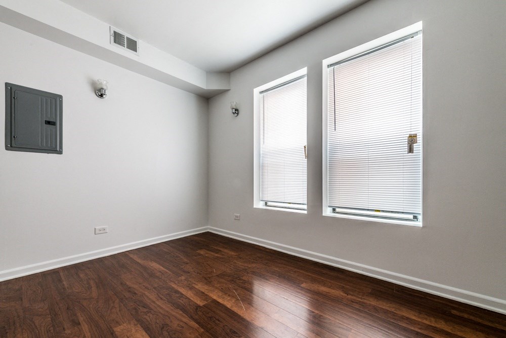 the living room of an apartment with wood flooring and two windows