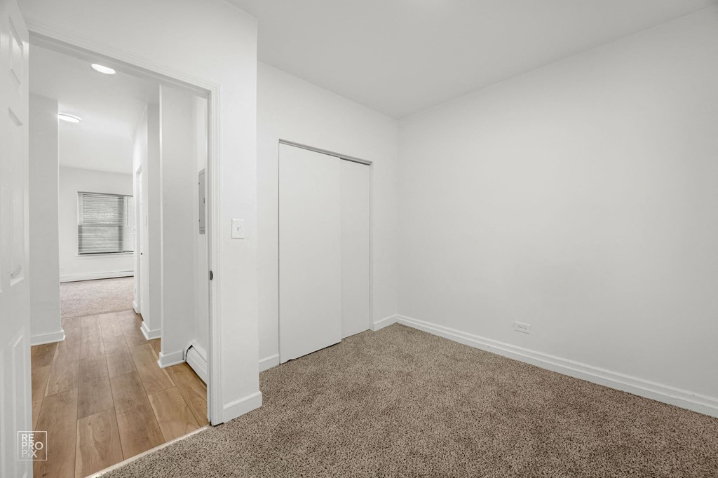 a bedroom with white walls and wood flooring and a closet
