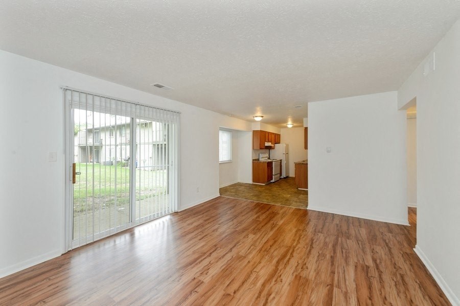 the living room and dining room of an apartment with wood floors and a glass door
