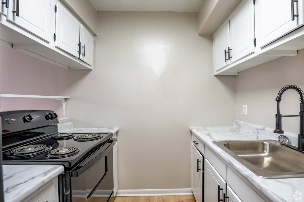 A kitchen with a stove, sink, and cabinets.